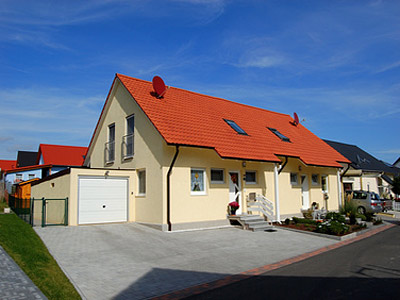 Ein modernes Einfamilienhaus mit rotem Dach und Garage, umgeben von einer gepflegten Auffahrt und Nachbarhäusern.